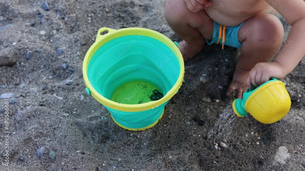 adorable baby boy playing on beach sea side with toy watering can and bucket.kid with sun cap on head sitting on sands or with feet in water. waves hitting legs.summer time vacation concept 4k adorable baby boy playing on beach sea side with toy watering can and bucket.kid with sun cap on head sitting on sands or with feet in water. waves hitting legs.summer time vacation concept 4k