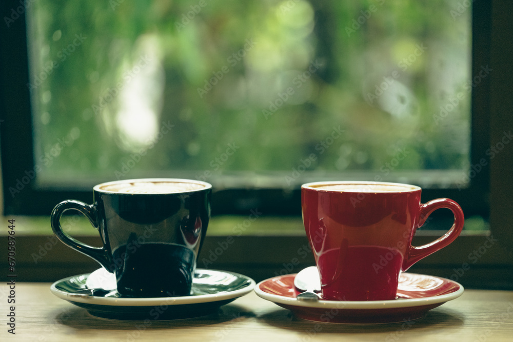 Two cup tea or coffee on wooden table side view window.Red and black hot coffee cup on the table by the window on a rainy day.Side view mugs on glass with reflection in the cafe on vintage style. Two cup tea or coffee on wooden table side view window.Red and black hot coffee cup on the table by the window on a rainy day.Side view mugs on glass with reflection in the cafe on vintage style.