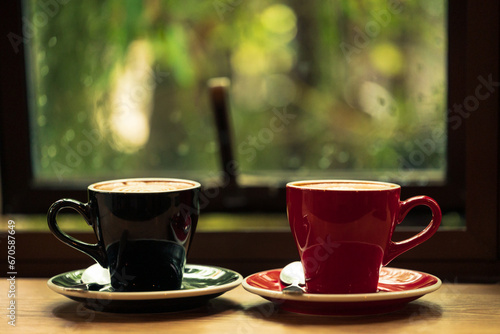 Two cup tea or coffee on wooden table side view window.Red and black hot coffee cup on the table by the window on a rainy day.Side view mugs on glass with reflection in the cafe on vintage style.