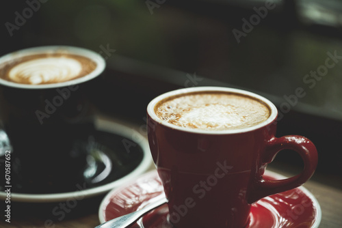 Fototapeta Naklejka Na Ścianę i Meble -  Two cup tea or coffee on wooden table side view window.Red and black hot coffee cup on the table by the window on a rainy day.Side view mugs on glass with reflection in the cafe on vintage style.