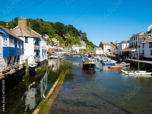 Sailing and fishing boats in harbour at the coastal village and port of Polperro on the south coast of Cornwall, UK. White and blue houses, hillside, clear blue sky.