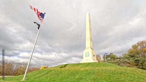 Historic Revolutionary War monument at Newtown Battlefield State Park with American flag blowing in the wind on hillside in New York State during Autumn Fall season color
