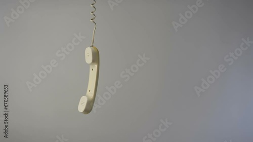 A white landline telephone handset hangs on a wire. Interrupted telephone conversation concept.