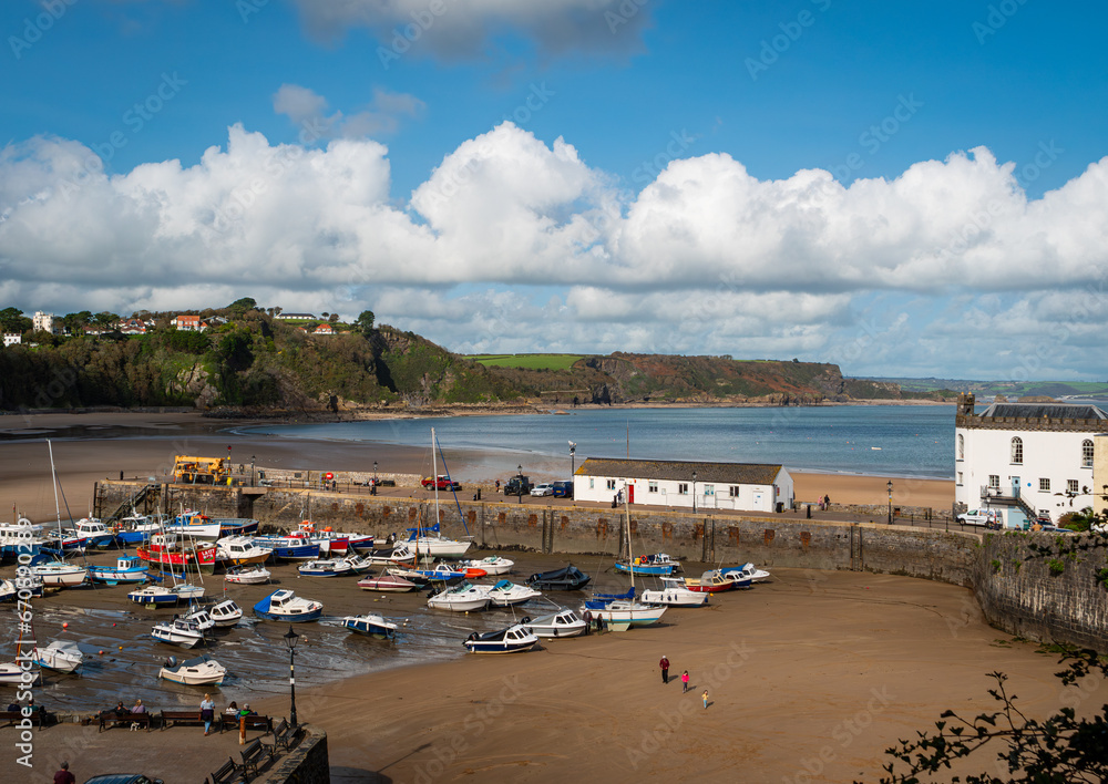 Sailing and fishing boats on wet sand, at low tide, in picturesque Tenby Harbour, on the Pembrokeshire coast of south Wales. Blue sky, white clouds.