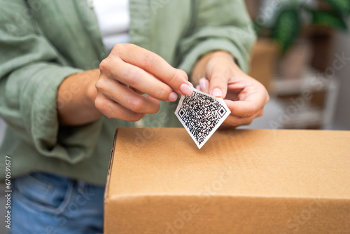 Female hands remove sticky part from sticker with barcode to send box of goods at workplace in premise woman employee marks cardboard parcel in post office photo