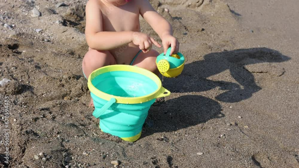 adorable baby boy playing on beach sea side with toy watering can and bucket.kid with sun cap on head sitting on sands or with feet in water. waves hitting legs.summer time vacation concept 4k adorable baby boy playing on beach sea side with toy watering can and bucket.kid with sun cap on head sitting on sands or with feet in water. waves hitting legs.summer time vacation concept 4k