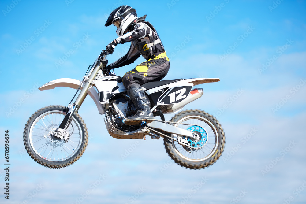 Person, motorcycle and air jump in blue sky as professional in action, competition or fearless. Bike rider, off road transportation stunt or fast speed adventure at rally, extreme sport or challenge