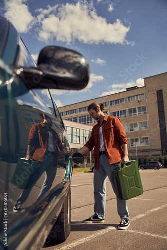 vertical shot of good looking sexy male model in stylish attire refueling his car with petrol