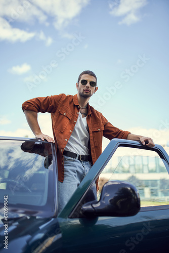 vertical shot of appealing young man in stylish vibrant clothing posing next to his car, fashion © LIGHTFIELD STUDIOS