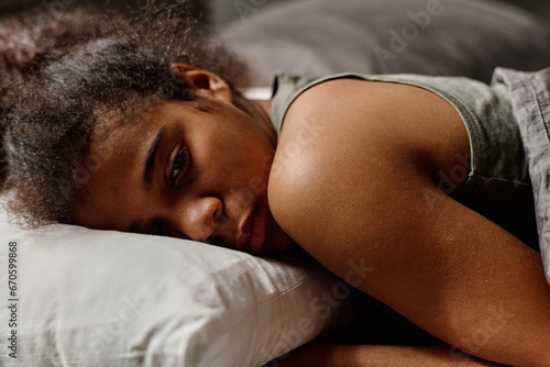 Fotografi Offended teenage girl in grey vest lying under blanket in bed and keeping head o
