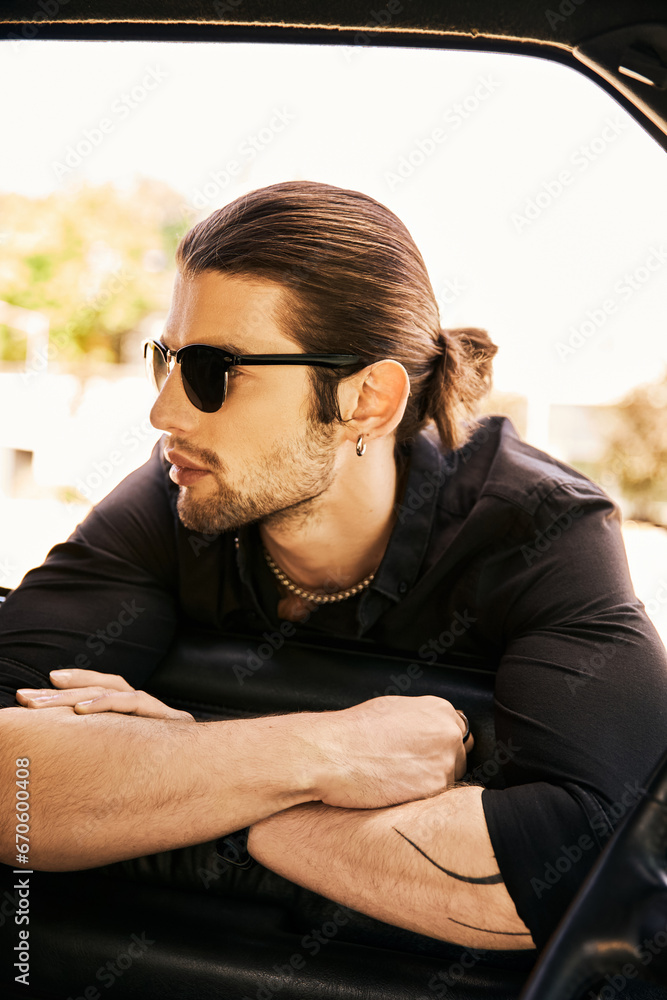 Obraz premium appealing sexy man with accessories in stylish black attire posing near his car and looking way