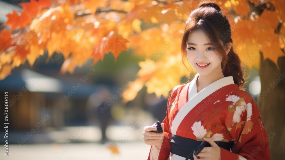 Young Asian woman in traditional kimono stands and smiles while looking at camera with phone on autumn maple leaves at park in Japan Young Asian woman in traditional kimono stands and smiles while looking at camera with phone on autumn maple leaves at park in Japan