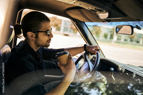 good looking man with ponytail behind steering wheel of his car with coffee in hand, sexy driver