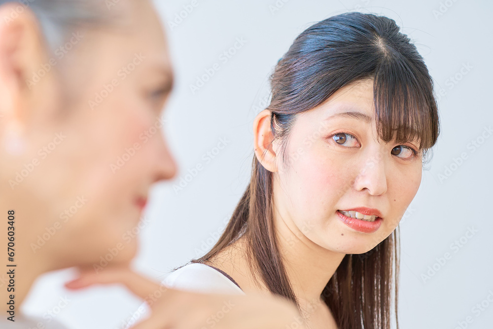 シニア女性の隣で、ストレスを感じる若い女性 シニア女性の隣で、ストレスを感じる若い女性