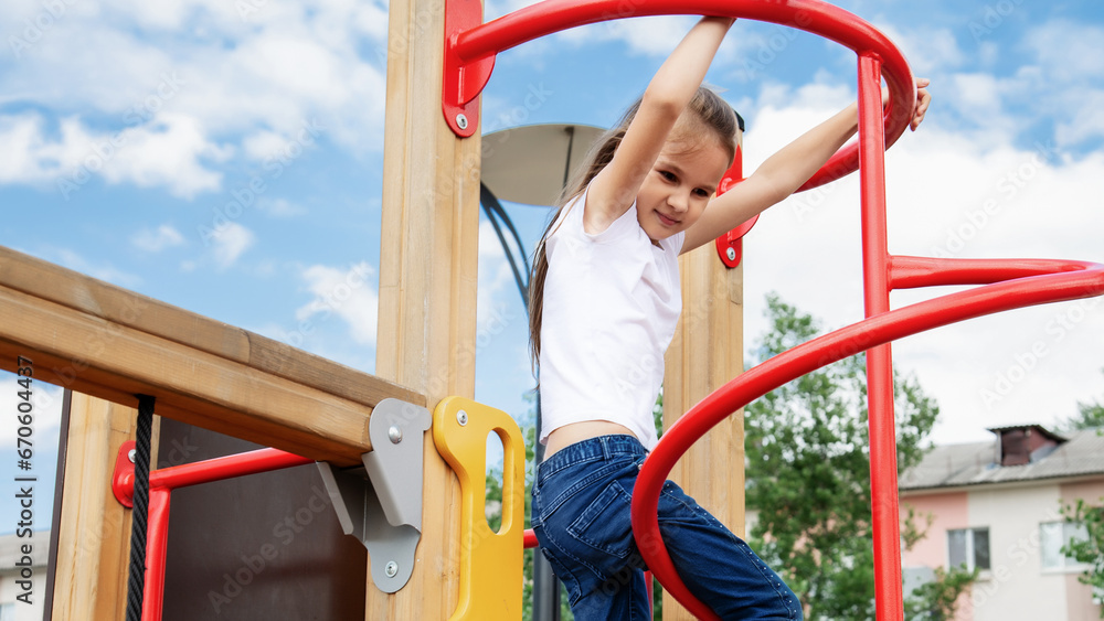 A playful little baby girl climbed an iron ladder on an outdoor playground. A cheerful preteen girl climbs the stairs on the playground. Games for the development of children outdoors.