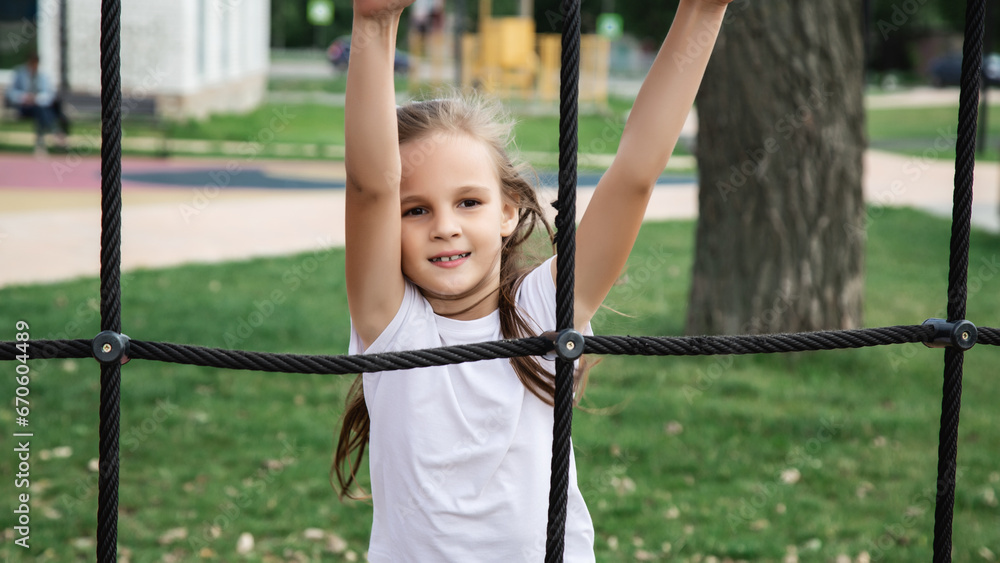 Active little child playing on rock climbing and jumping on school yard playground. Children play and climb outdoors on a sunny summer day.