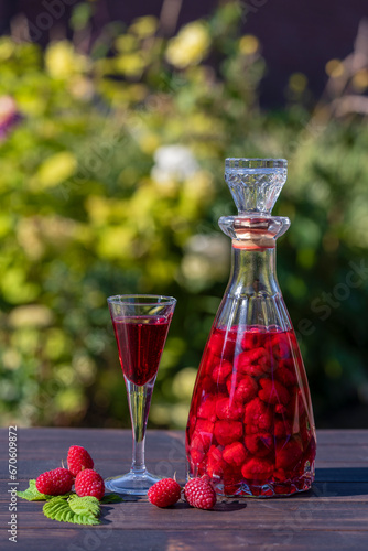 Homemade red raspberry brandy in glasses and in a glass bottle on a wooden table in a summer garden, closeup
