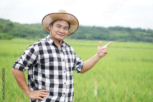 Handsome Asian man farmer is at paddy field, wears hat and plaid shirt, put hat on waist, point finger up. Concept, Agriculture occupation. Thai farmer. Working with nature. Organic farming.     