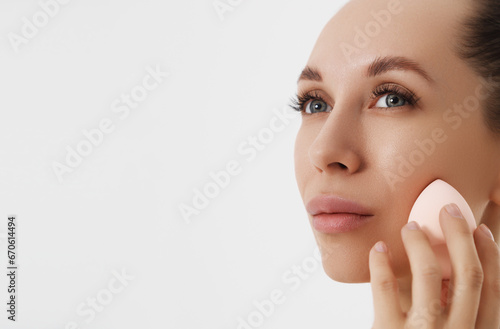 Closeup portrait of a woman applying dry cosmetic tonal foundation using makeup sponge on the face using makeup brush.  © looking2thesky