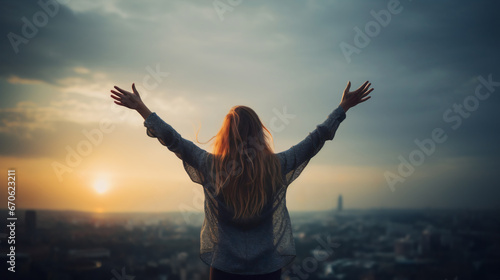 A young woman stands with outstretched arms, embracing the dawn as the sun rises over a vast cityscape. Concept of confidence and renewal, symbolizing hope, strength, determination, a new beginning photo
