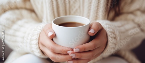  Woman's hands in white knitted sweater holding cup of coffee. Christmas winter design.