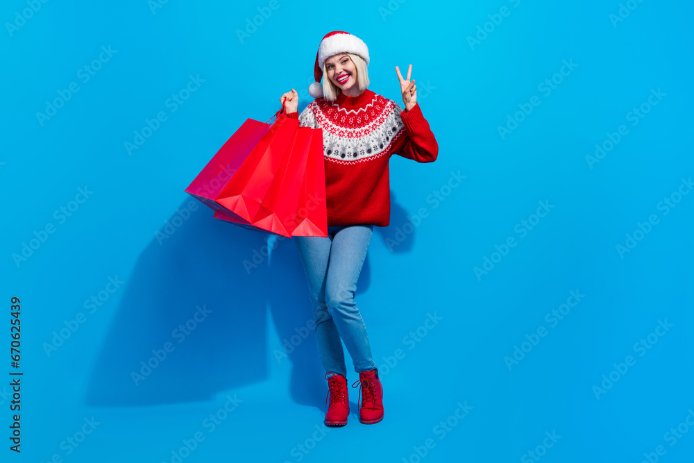 Obraz premium Full length photo of pretty shiny lady santa helper dressed ornament sweater showing v-sign buying xmas gifts isolated blue color background