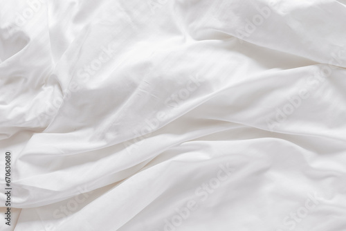 White fabric texture background, wavy cloth. Crease bedclothes fragment as background, Crumpled sheet of Morning bed. White bed linen as minimalistic backdrop. Top view aesthetic surface