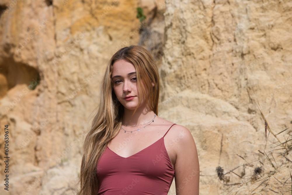 pretty young woman in red summer dress is posing on the cliff. The woman makes different body expressions. In the background rocks and vegetation.