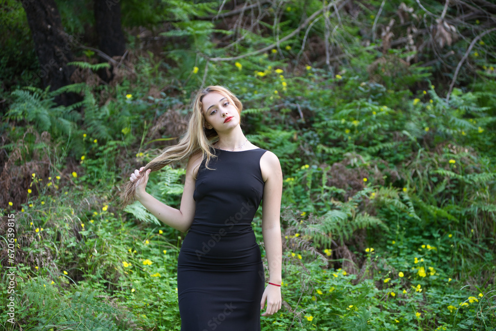Young, beautiful blonde woman dressed in black walks through the forest in different postures and expressions. In the background ferns and yellow flowers. Concept expressions in nature. Young, beautiful blonde woman dressed in black walks through the forest in different postures and expressions. In the background ferns and yellow flowers. Concept expressions in nature.
