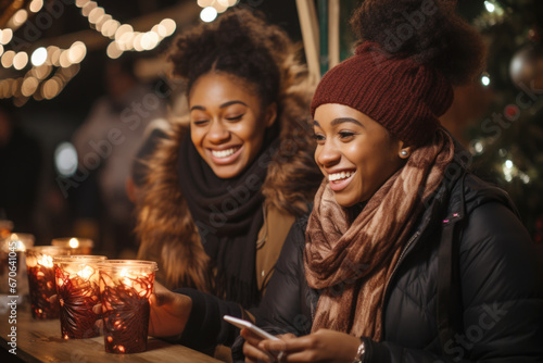 Two beautiful black female friends having god time on traditional Christmas market, drinking hot beverages on winter evening