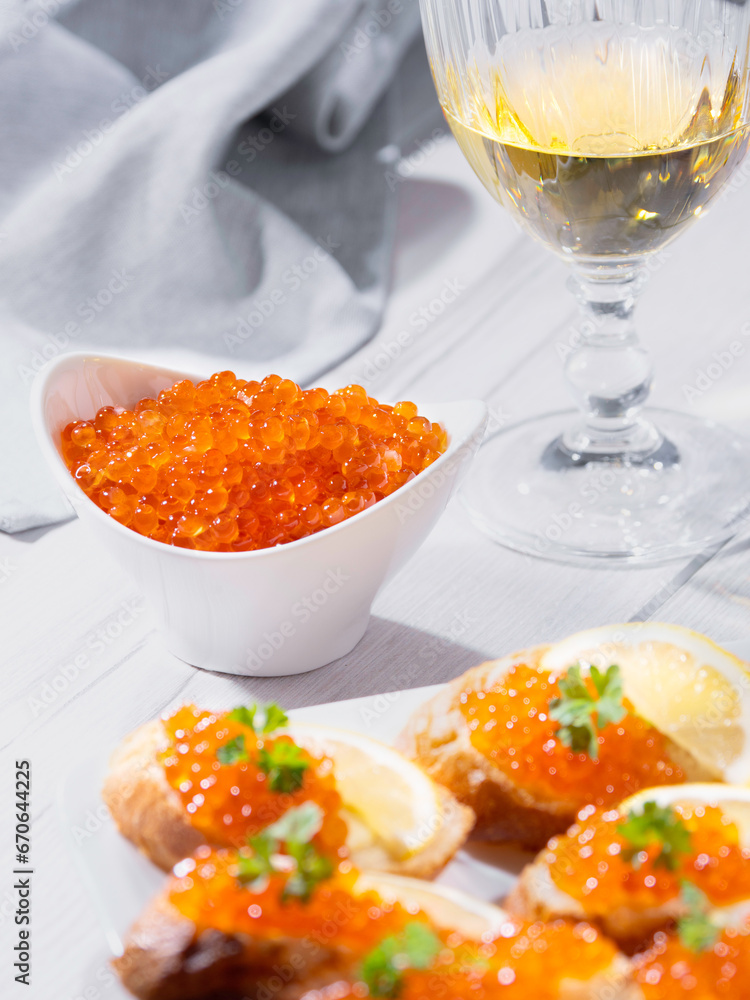 Salmon caviar in a white bowl and sandwiches with red caviar with white wine. Gourmet food up close. Seafood and delicatessen.