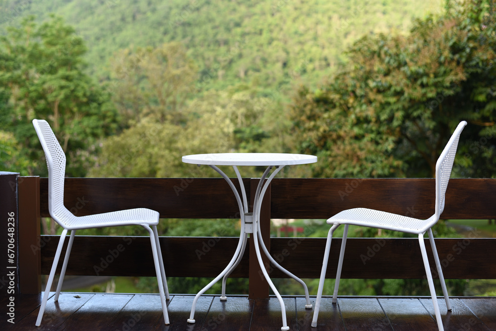 White metal chair on black wooden terrace with blurry lush forest view background