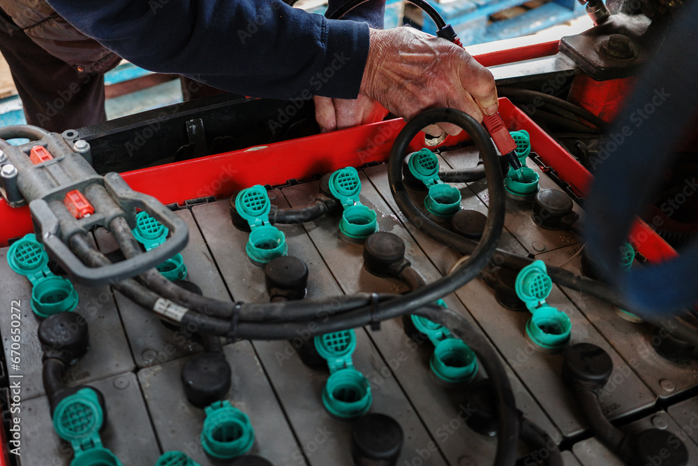 Forklift truck electric batteries being topped up at the regular maintenance check mans hand closeup with water hose - obrazy, fototapety, plakaty 