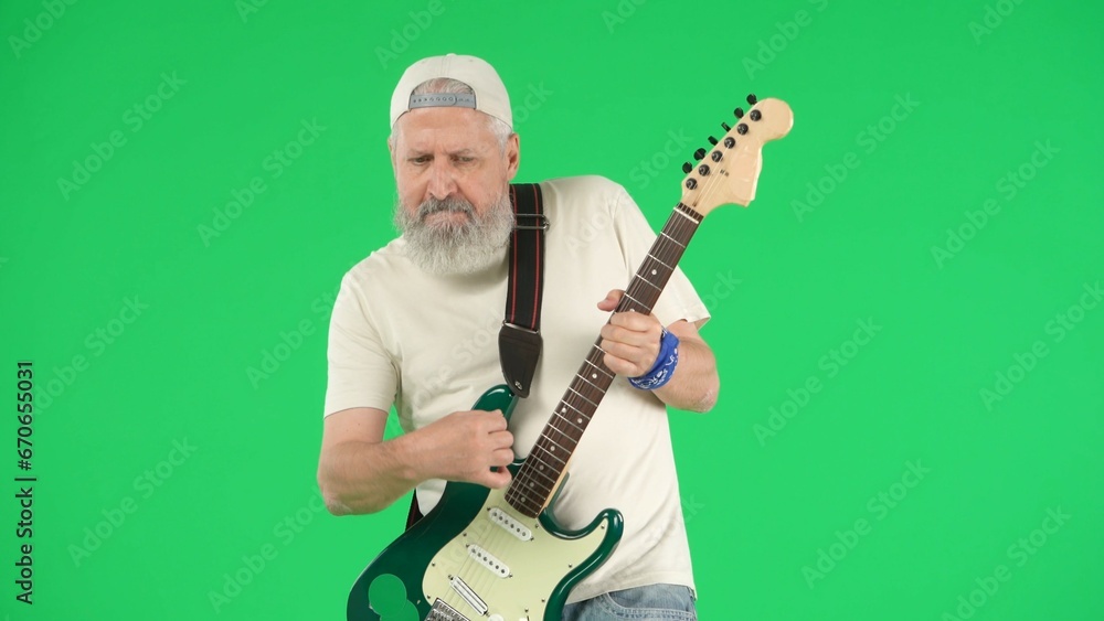 Obraz premium Portrait of senior man hipster on Chroma key green screen background, man in white t-shirt playing on electric guitar at camera. Advertising area, workspace mockup.