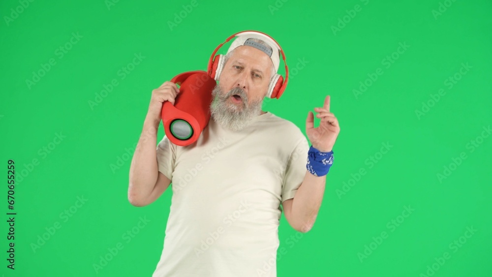 Portrait of senior man hipster on Chroma key green screen background, man in white t-shirt and headphones holding music speaker. Advertising area, workspace mockup. Portrait of senior man hipster on Chroma key green screen background, man in white t-shirt and headphones holding music speaker. Advertising area, workspace mockup.