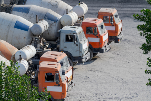 Close-up side view of group of concrete mixer trucks standing parked on ground in a sunny summer day. Soft focus. Copy space for your text. Construction industry theme.