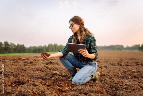 Young woman agronomist checks the quality of the soil before sowing. Farmer woman with a digital tablet holds black soil in her hands. Concept of technology, ecology.
