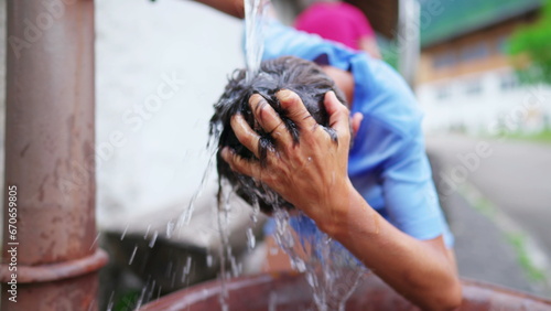 Young boy washing head and hair at public fountain street in Europe during hot summer day. Teen kid refreshing himself feeling the water pour in slow-motion