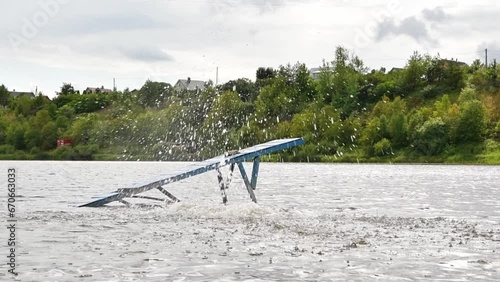 Girl jumps from a wooden footbridge into the river on a sunny summer day.
