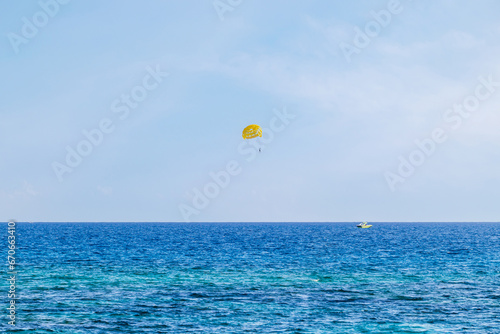 View of the sea with turquoise water and a yellow parasailing parachute being pulled by a motorboat. Active recreation on the water photo