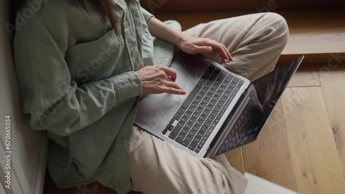 Close up top view young woman hands typing on laptop computer sitting cross legged on floor near window at home office