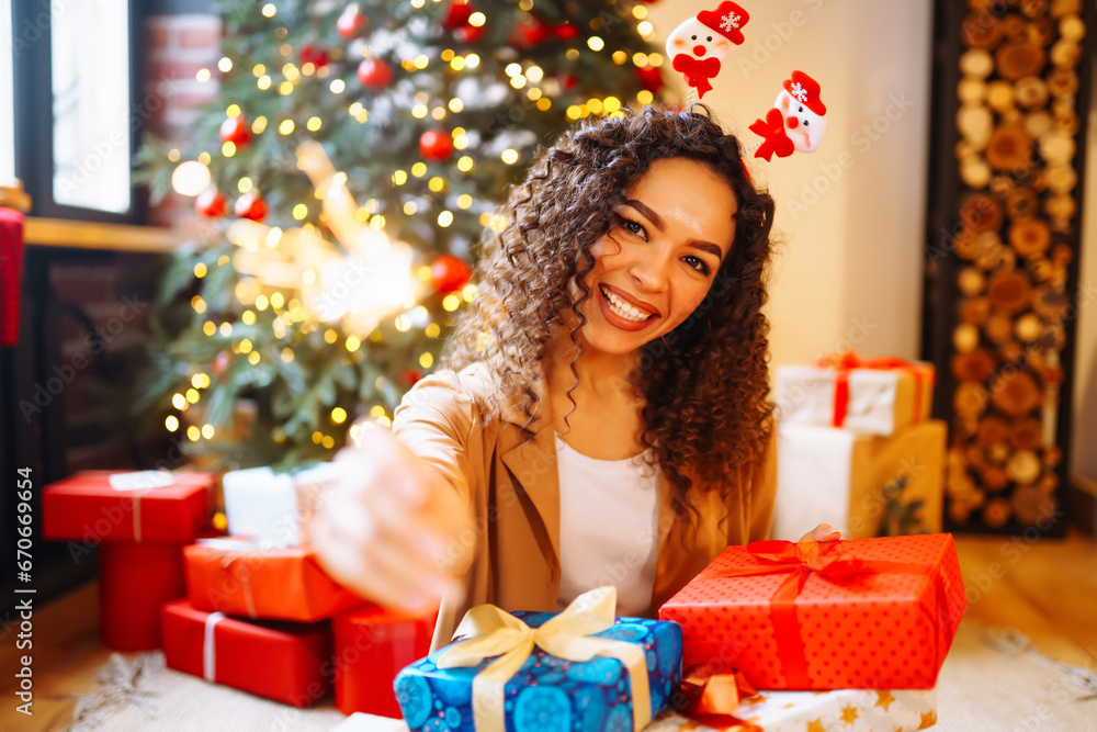Happy woman holding sparkler and Christmas gifts at home near New Year tree. Holiday concept. The winter vacation.