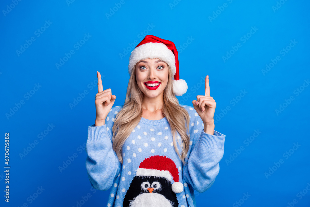 Obraz premium Photo portrait of pretty blonde young girl excited finger point up dressed penguin sweater x-mas hat isolated on blue color background