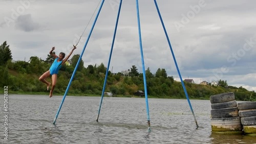 Little girl jumps from a wooden bungee into the river on a sunny summer day.