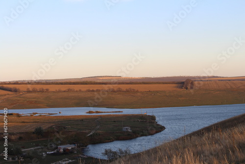 A landscape with a body of water and a land with trees and a rainbow in the sky