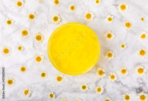 Chamomile body scrub with herbal chamomile extract on a textured background. Skin softening scrub. Body care cosmetics, natural organic product, herbal medicine. Beauty concept. Place for text.