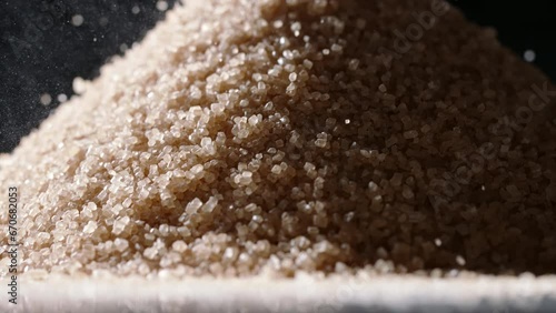 Brown cane sugar is poured on table. Close up slow motion black background. Be mindful of sugar intake to fend off obesity, diabetes, and other diseases that plague our society. Nutrition diet modern