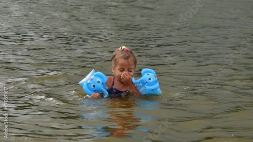 CLOSE UP: Cute little girl in the pool river with arm floats. Adorable girl practicing swimming with water wings in river. Enjoyful refreshment on a hot and sunny summer day.