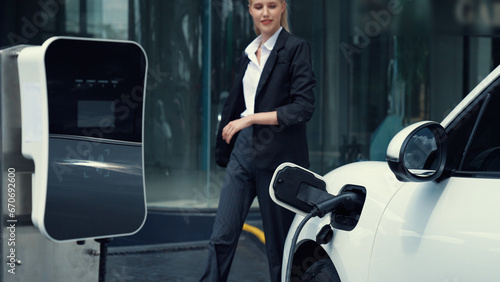 Progressive businesswoman unplug charger plug from charging station to his electric car before driving around city center. Eco friendly rechargeable car powered by sustainable and clean energy. photo