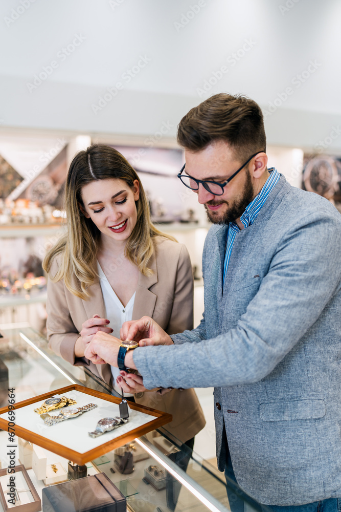 Fototapeta premium Elegant middle age businessman choosing and buying his new expensive watch. Beautiful young female seller helps him to make good decision. Fashion style and elegance concept.